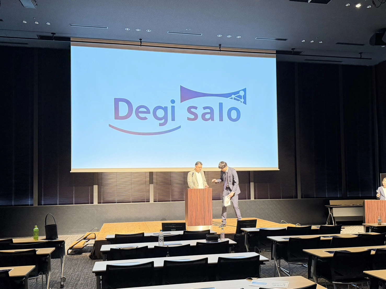 Degi saloのロゴが映し出された会場ステージで、登壇者が講演準備