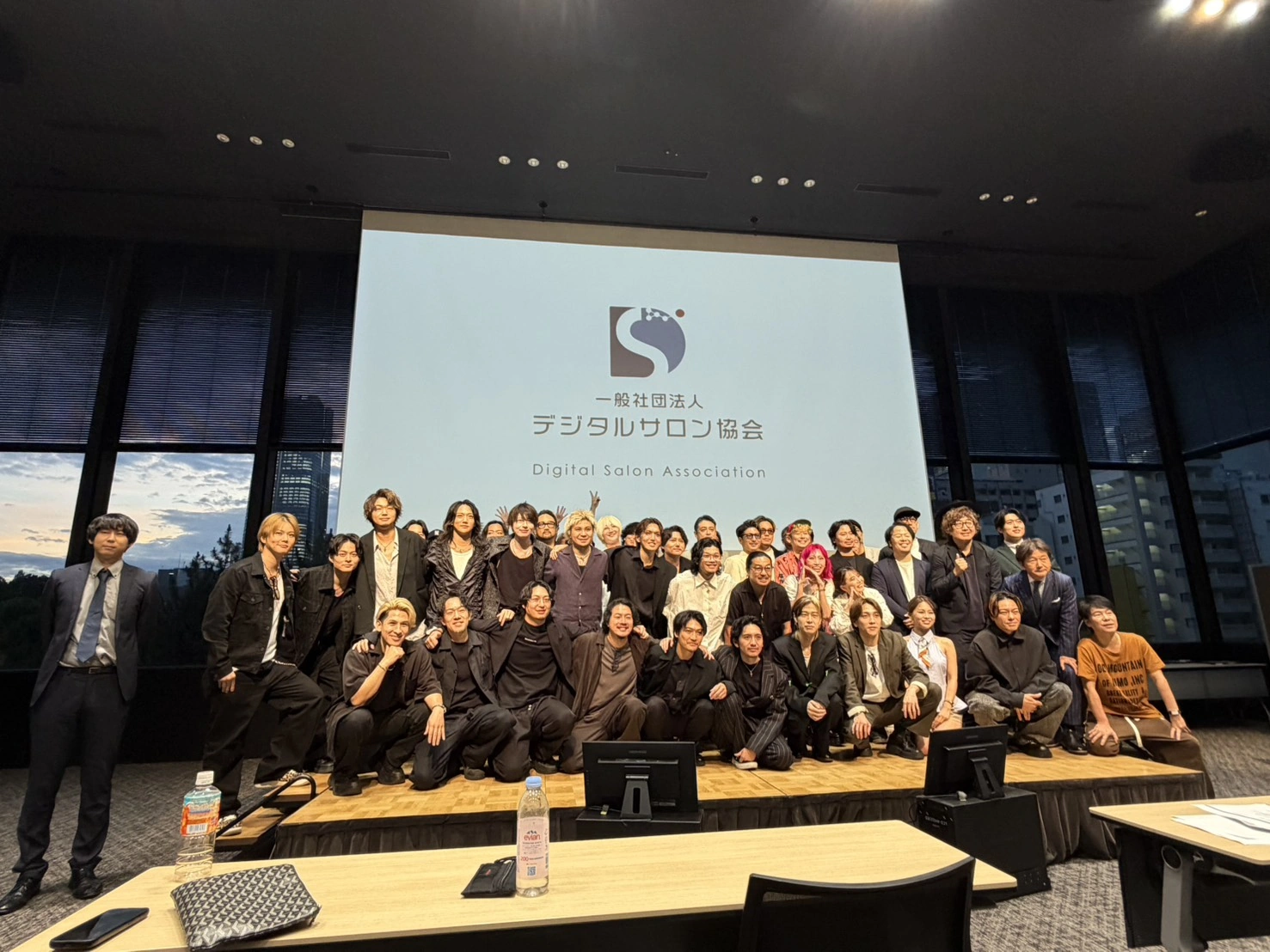 デジタルサロン協会のロゴが映し出された会場ステージ前で、参加者が集合写真を撮影している様子